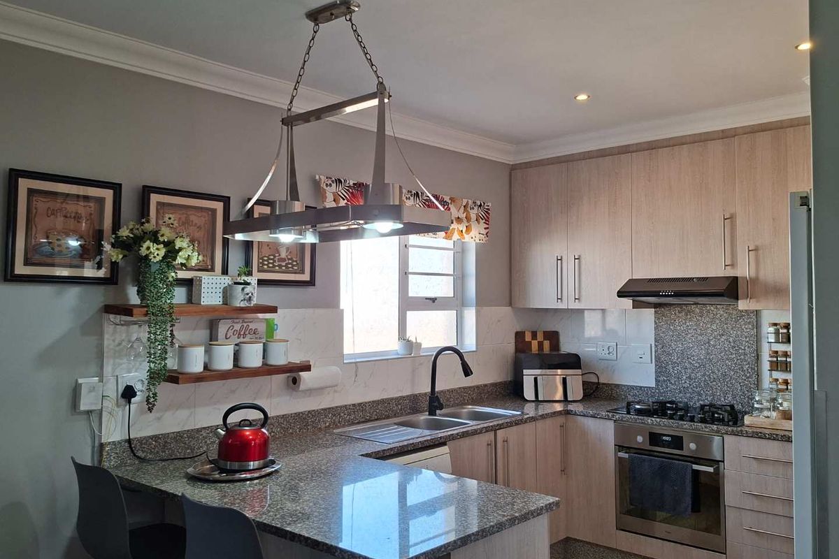 Modern kitchen featuring light wood cabinetry, granite countertops, a built-in oven with gas hob, extractor fan, and a breakfast bar with pendant lighting.