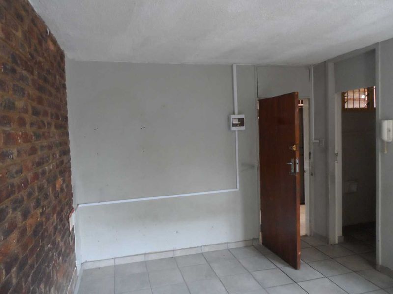 An empty entrance area featuring tiled flooring, an exposed brick feature wall, and a functional intercom system, providing a blank canvas for renovation.