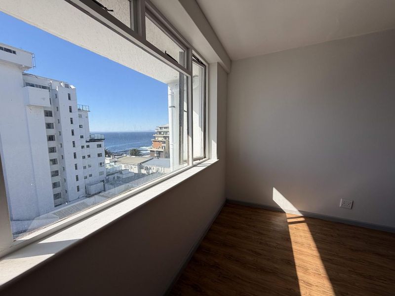 A bright, empty bedroom featuring laminate flooring and a large window offering expansive coastal and urban views.