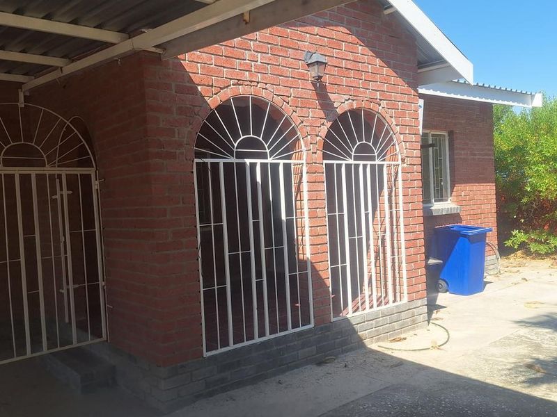 Rear exterior view of a face brick house featuring a covered carport area, security gates, and concrete paving.