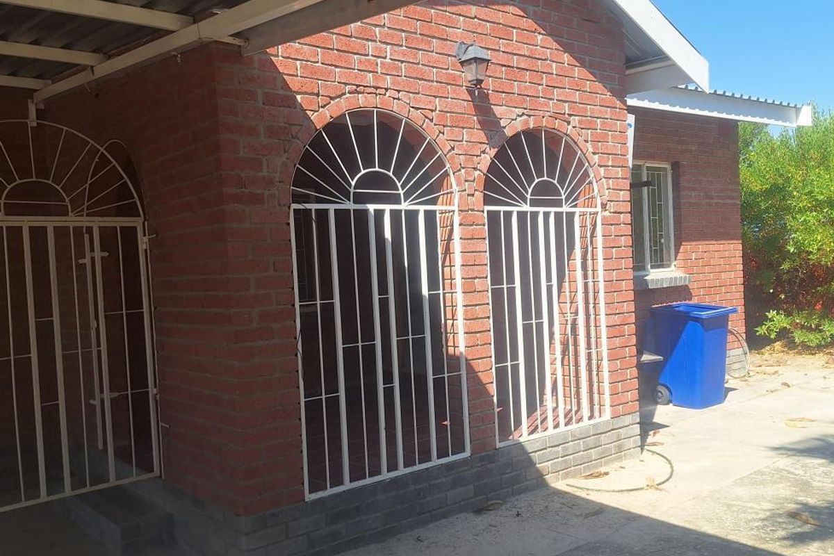 Rear exterior view of a face brick house featuring a covered carport area, security gates, and concrete paving.