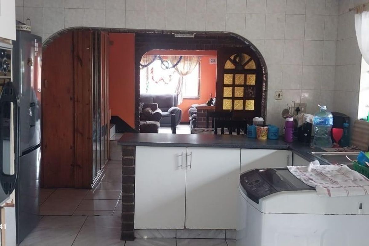 A dated kitchen featuring tiled walls and flooring, built-in oven, and an arched opening leading to the adjacent living area.
