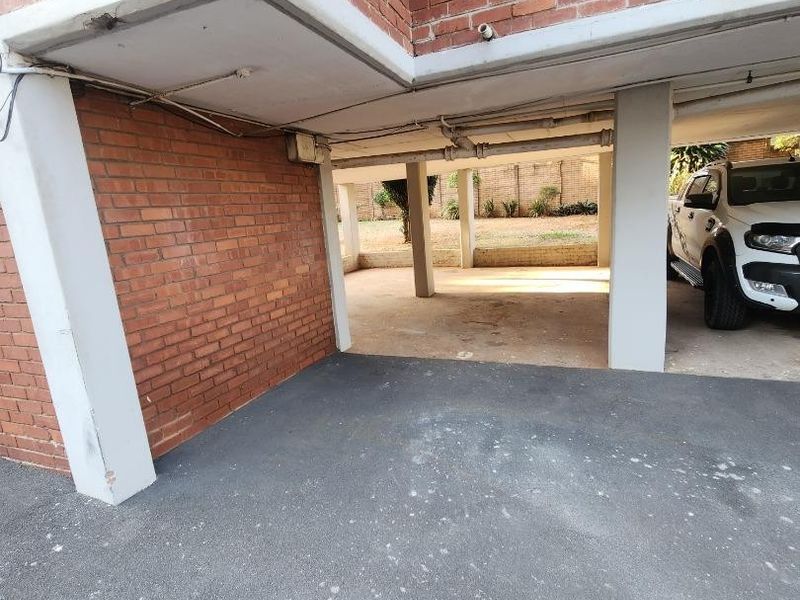 A covered parking area featuring exposed brick walls and concrete structural pillars, providing functional off-street parking space.