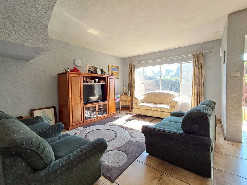 A living room featuring tiled flooring, textured walls, and a large window providing natural light.