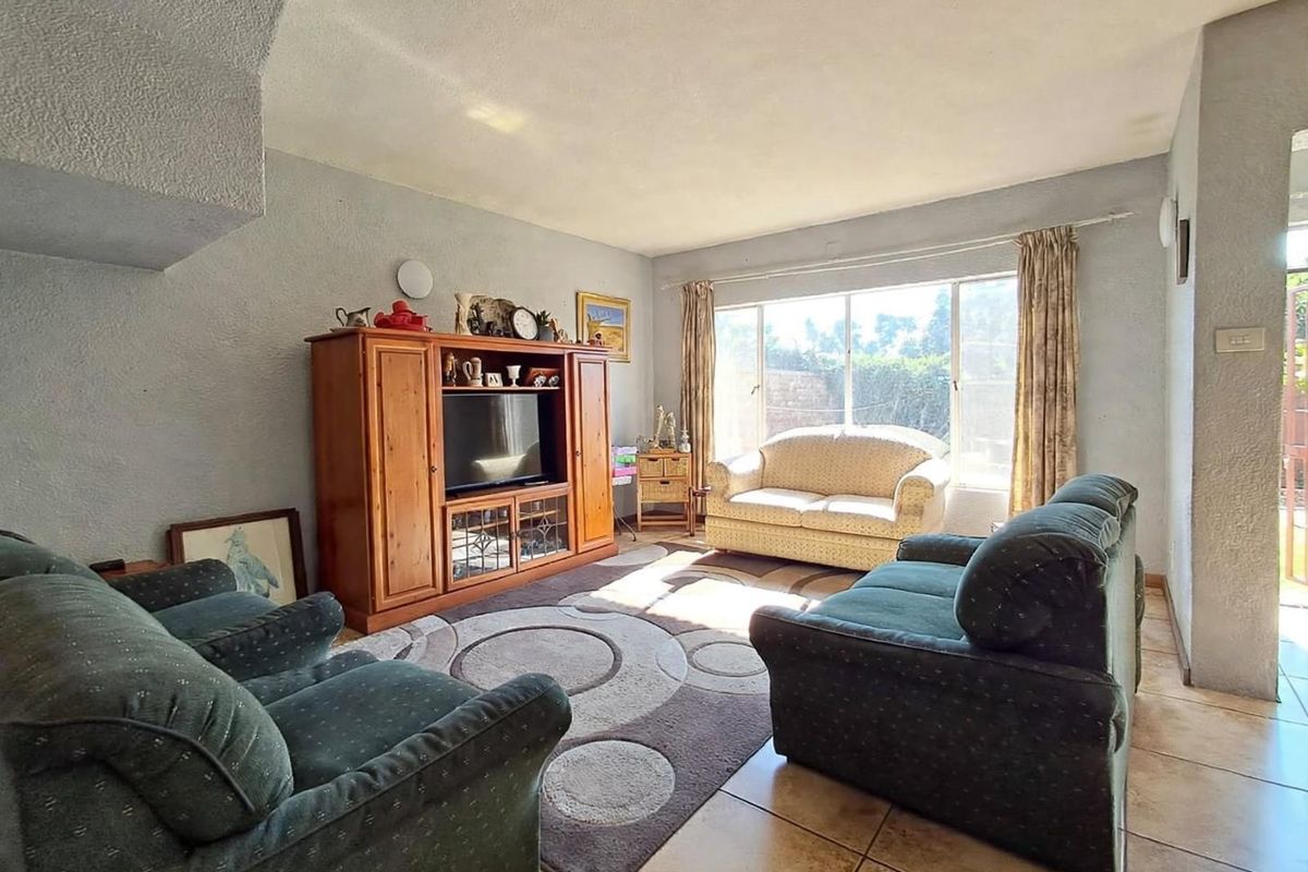 A living room featuring tiled flooring, textured walls, and a large window providing natural light.