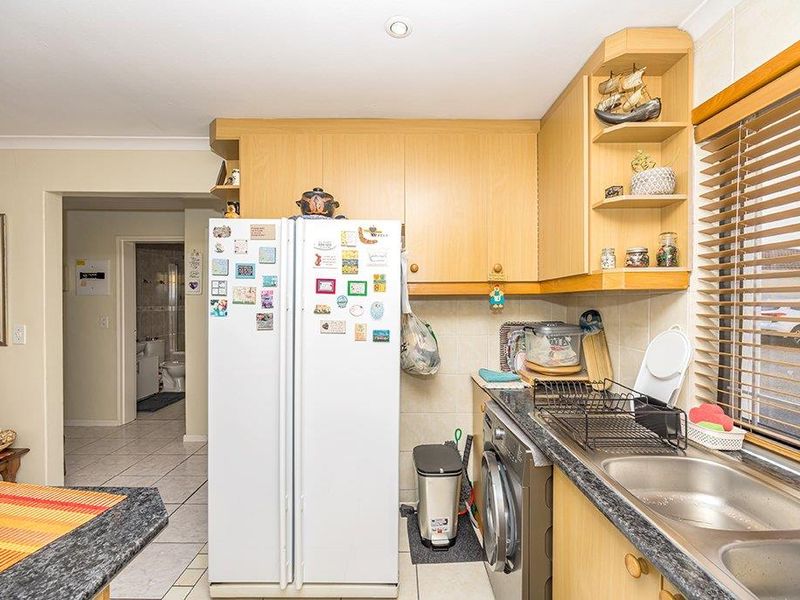 Functional kitchen featuring laminate cabinetry, double bowl stainless steel sink, and tiled splashback, with an adjacent view into the bathroom area.