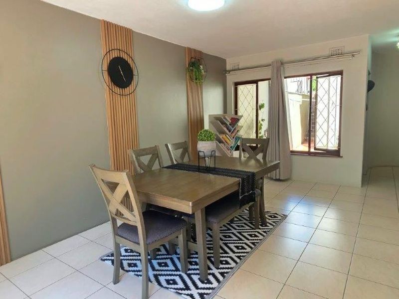 A well-maintained dining area featuring neutral wall tones, decorative slat wall paneling, and light-colored ceramic floor tiles with access to an outdoor space.