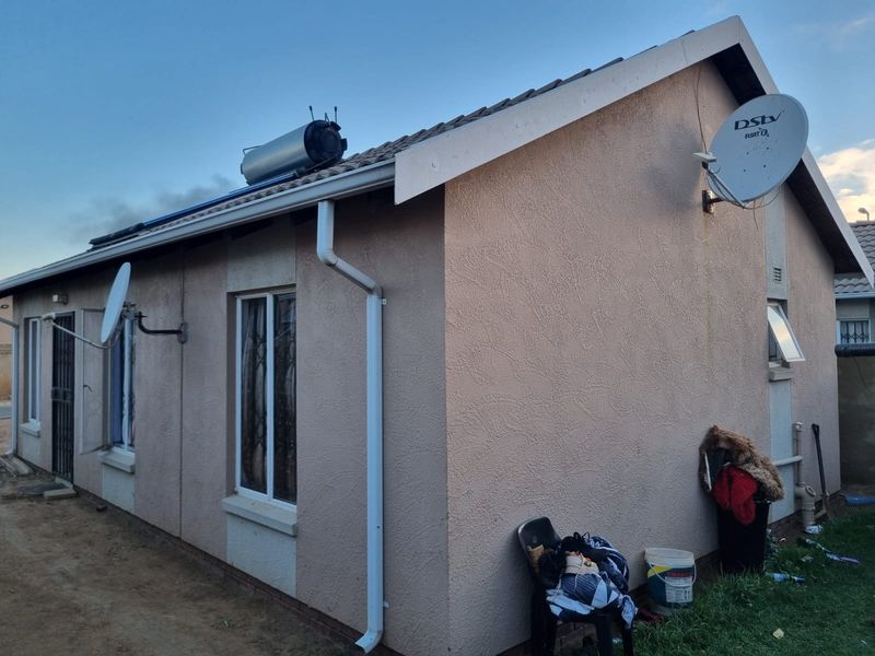Rear exterior view of the house featuring a solar water heater, satellite dish, and standard plastered wall finish with security bars on windows.