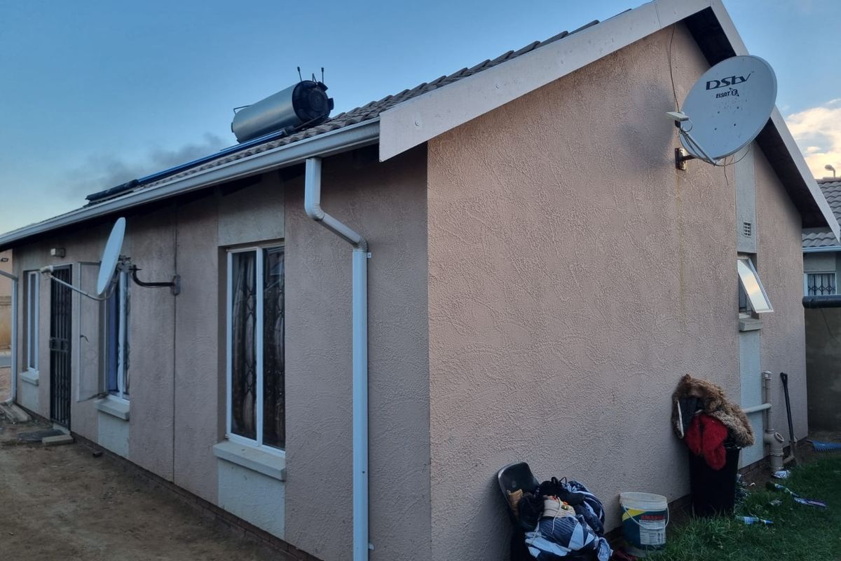 Rear exterior view of the house featuring a solar water heater, satellite dish, and standard plastered wall finish with security bars on windows.