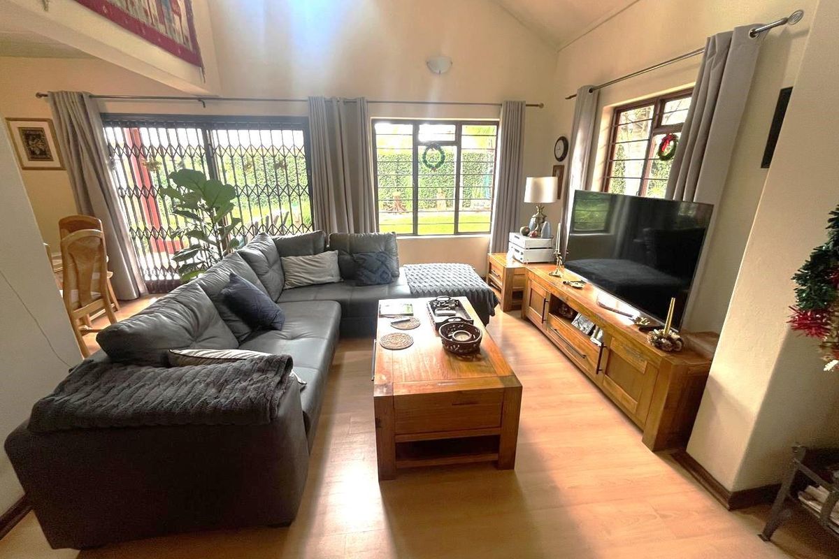 Spacious living room featuring high vaulted ceilings, laminate flooring, and large windows providing ample natural light with access to the outdoor area.