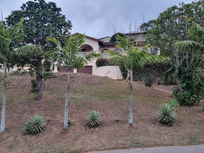 Front elevation of a residential property featuring a double garage, elevated balcony, and established garden landscaping on a sloped plot.
