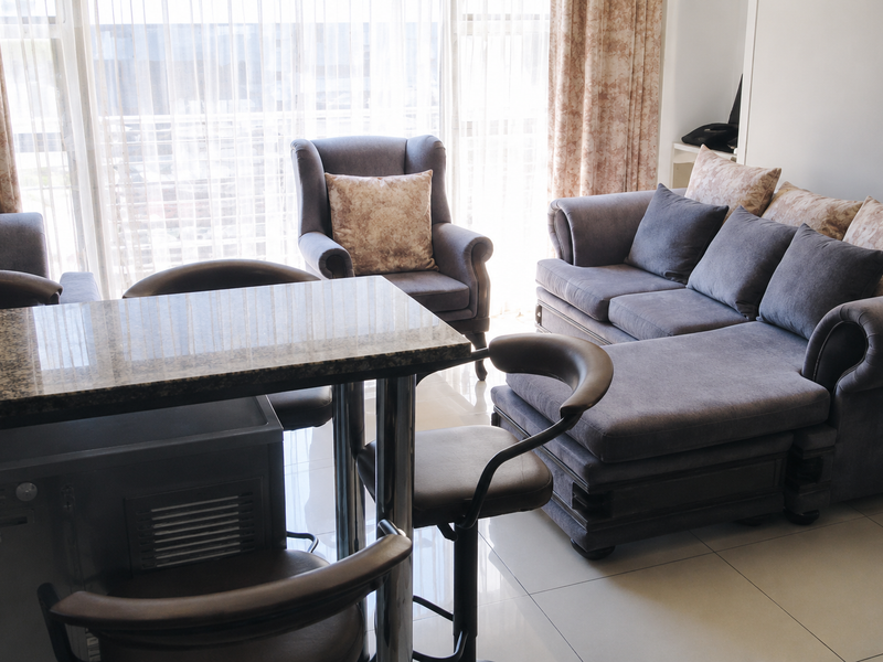An open-plan living and dining area featuring tiled flooring, a granite-topped breakfast bar, and large sliding glass doors providing natural light.