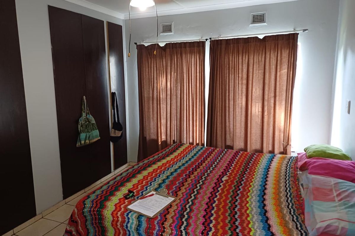 A bedroom featuring built-in dark wood cabinetry, tiled flooring, and large windows with curtain tracks.