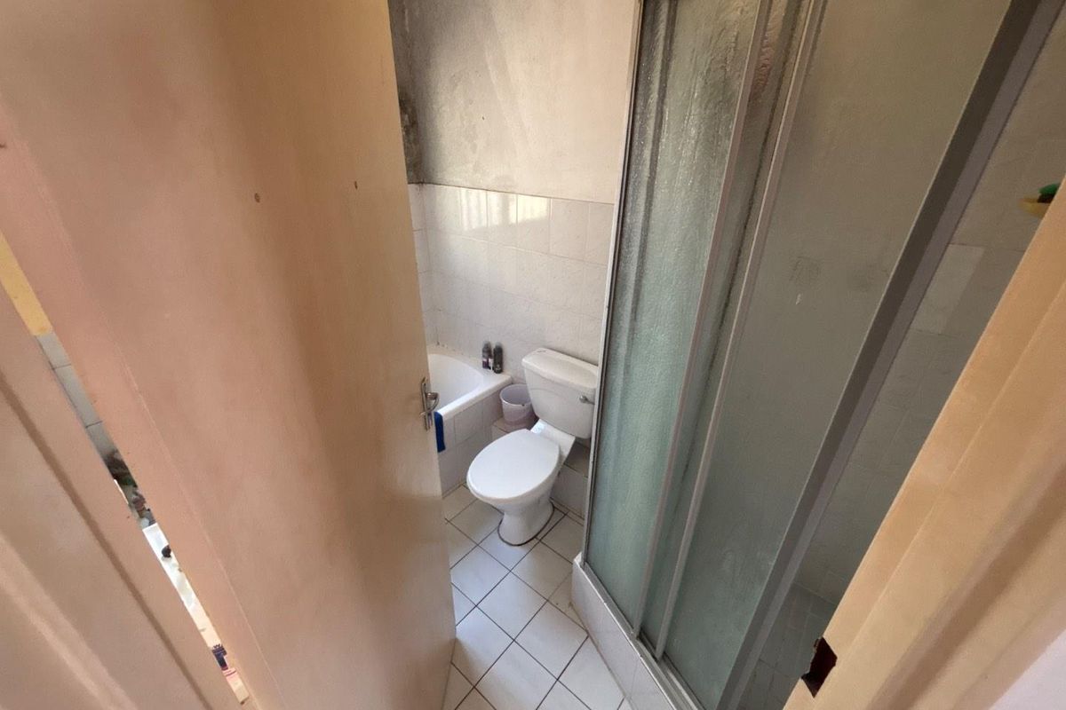 A compact bathroom featuring a shower enclosure, bathtub, and toilet, currently requiring cosmetic updates and wall finishing to improve its overall condition.
