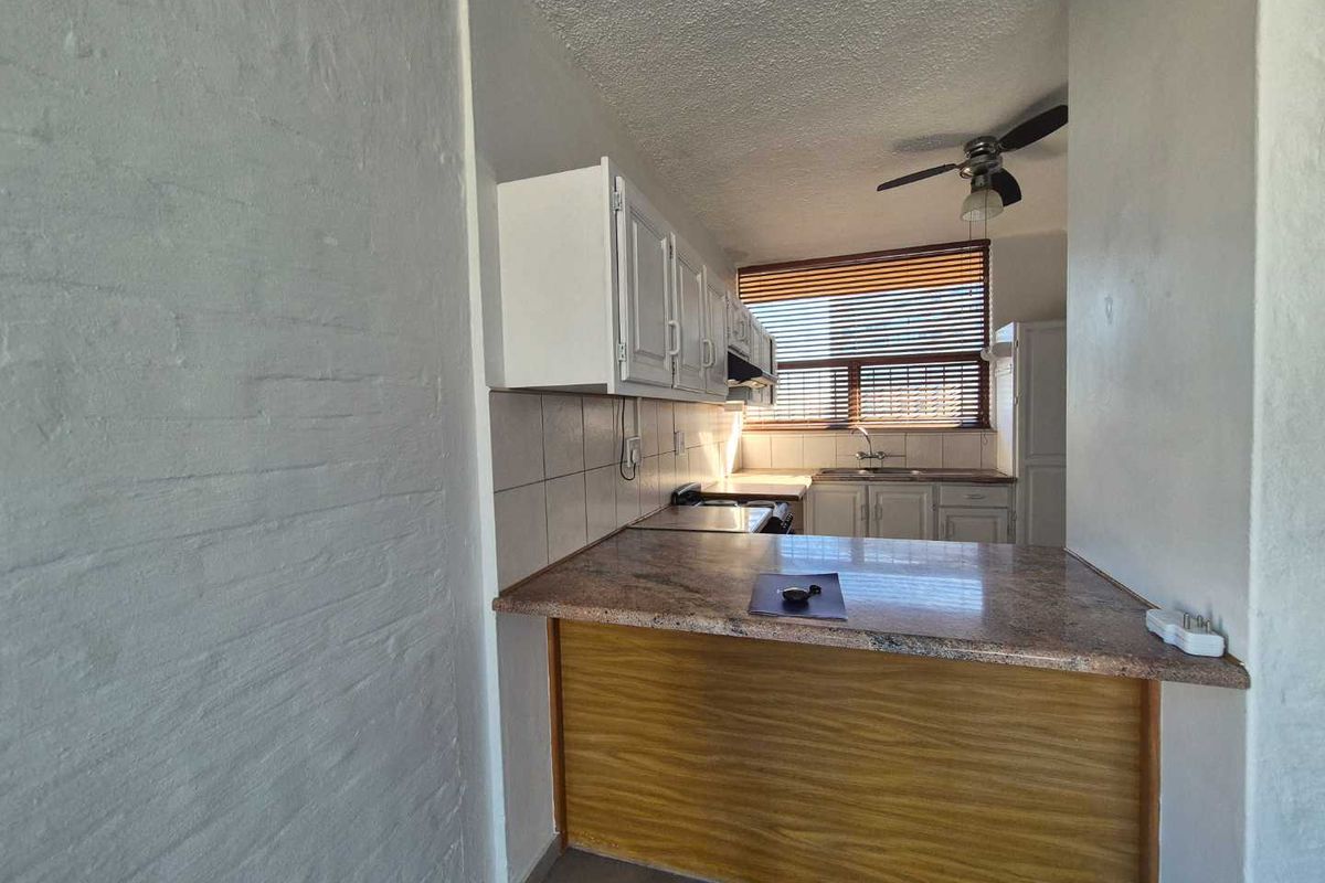 A compact kitchen featuring a breakfast bar, tiled backsplash, built-in cabinetry, and a ceiling fan, offering a functional layout for daily use.