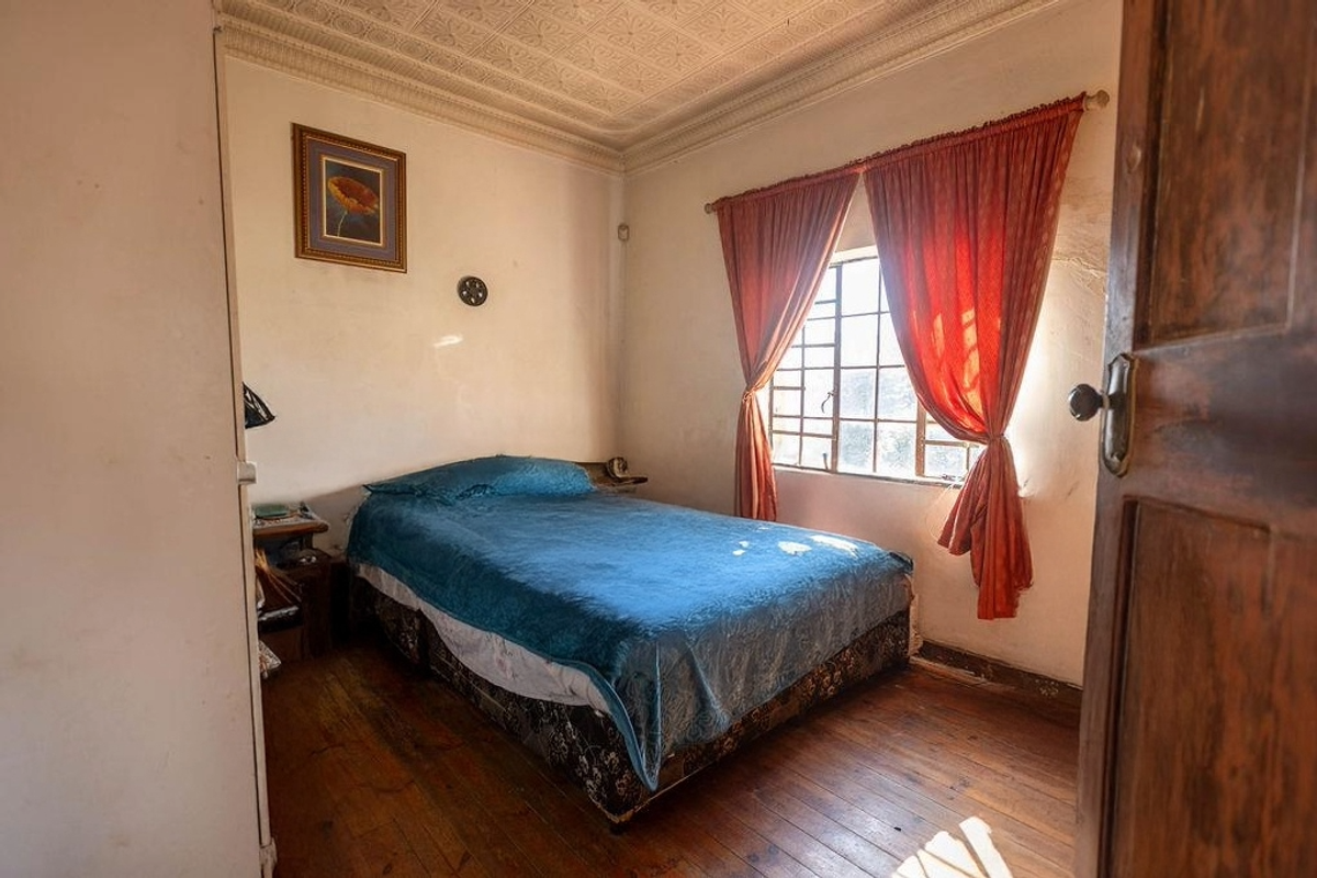 A bedroom featuring original pressed metal ceilings, timber flooring, and a metal-framed window, requiring cosmetic updates to restore its character.