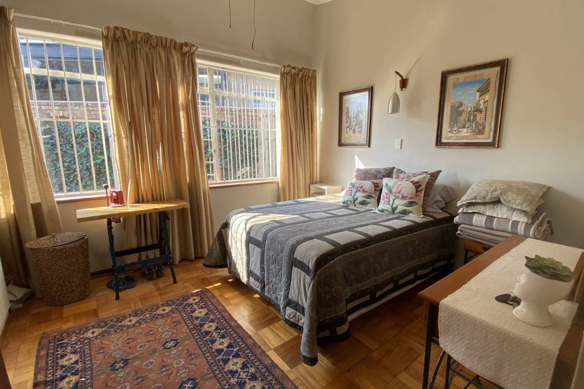 A bedroom featuring classic parquet flooring, large windows with security bars, and decorative wall-mounted lighting.
