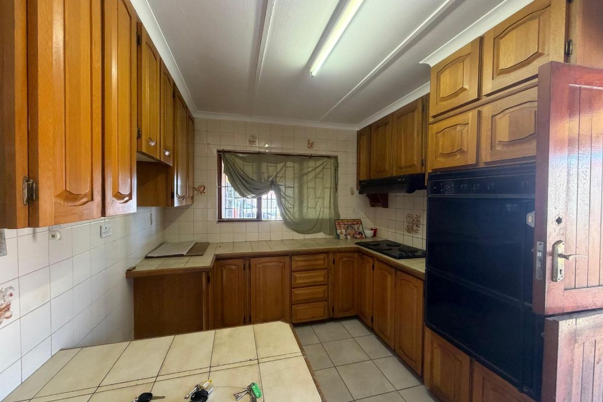 A functional kitchen featuring traditional wooden cabinetry, tiled countertops, built-in oven, and hob, offering a classic layout with ample storage space.