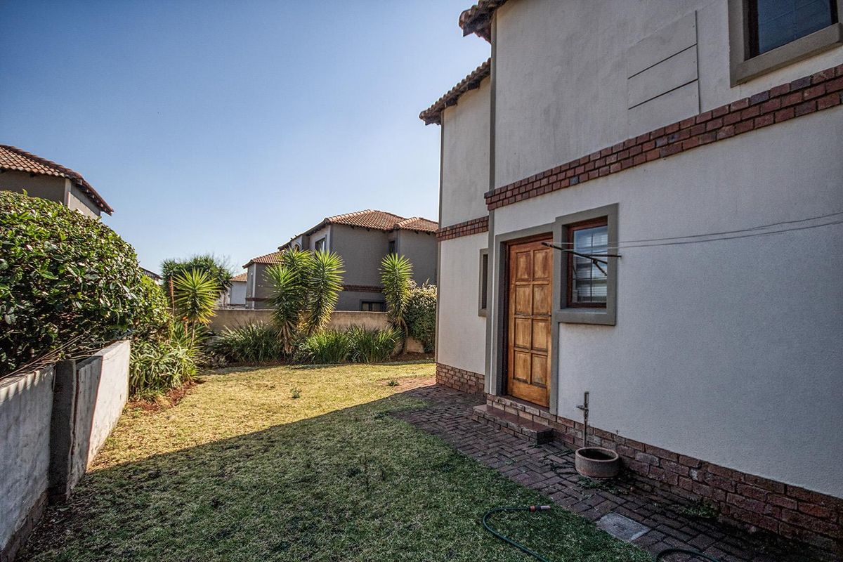 A view of the rear garden featuring a paved walkway, established landscaping, and a rear access door to the property.