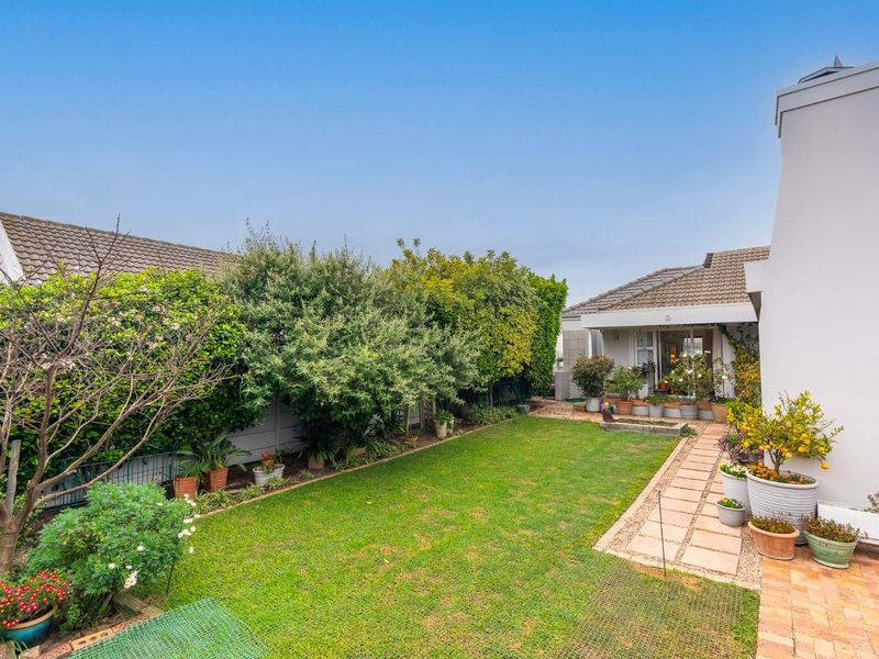 A well-maintained rear garden featuring a paved walkway, established greenery, and a prominent external chimney on the side of the house.