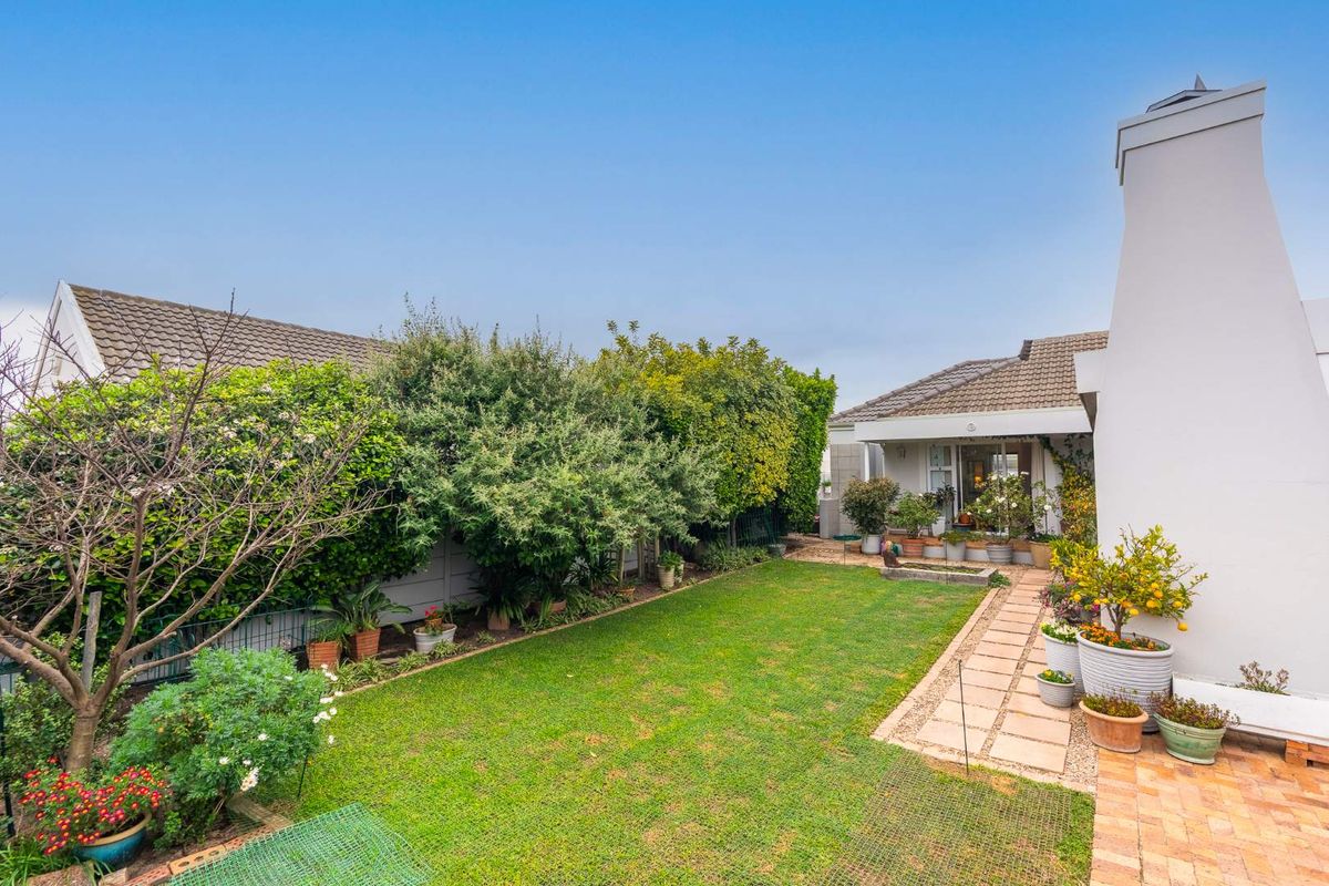 A well-maintained rear garden featuring a paved walkway, established greenery, and a prominent external chimney on the side of the house.