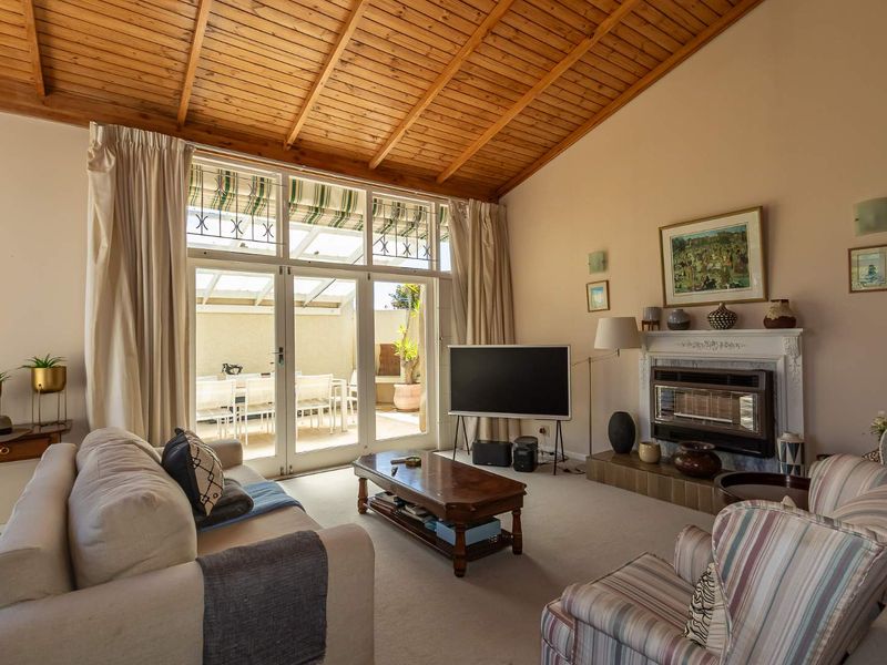 Spacious living room featuring a vaulted timber ceiling, a built-in fireplace, and large french doors providing direct access to an outdoor patio area.