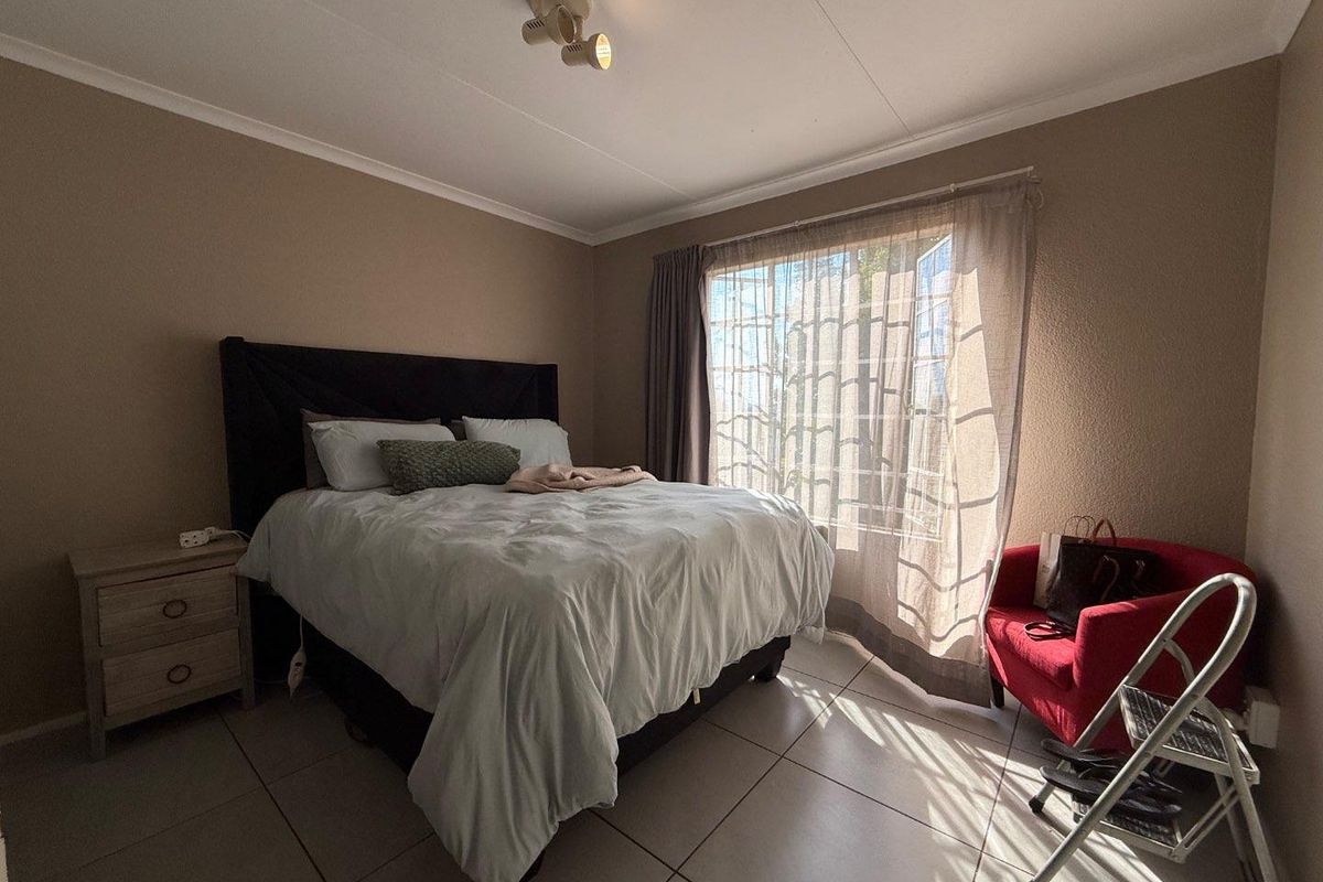 A bedroom featuring tiled flooring, neutral wall tones, and a large window allowing natural light, providing a comfortable and functional living space.