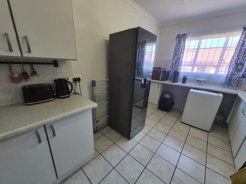 A functional kitchen featuring white cabinetry, laminate countertops, tiled flooring, and a tiled backsplash, offering a practical layout for daily meal preparation.