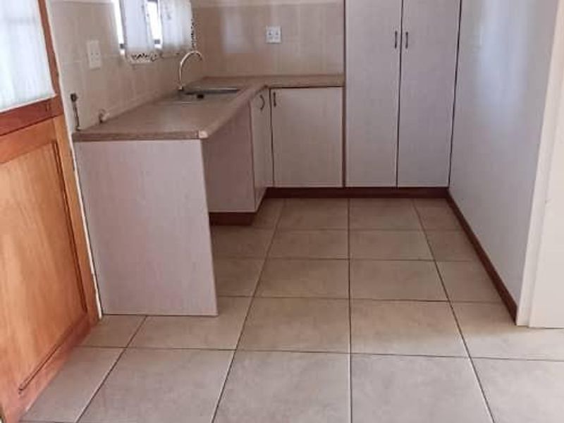 A compact, functional kitchen featuring tiled flooring, built-in cabinetry with laminate countertops, and a stainless steel sink.