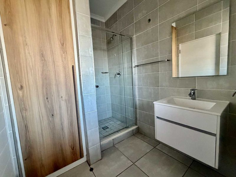 Modern bathroom featuring a glass shower enclosure, wall-mounted vanity with basin, and neutral grey wall and floor tiling.
