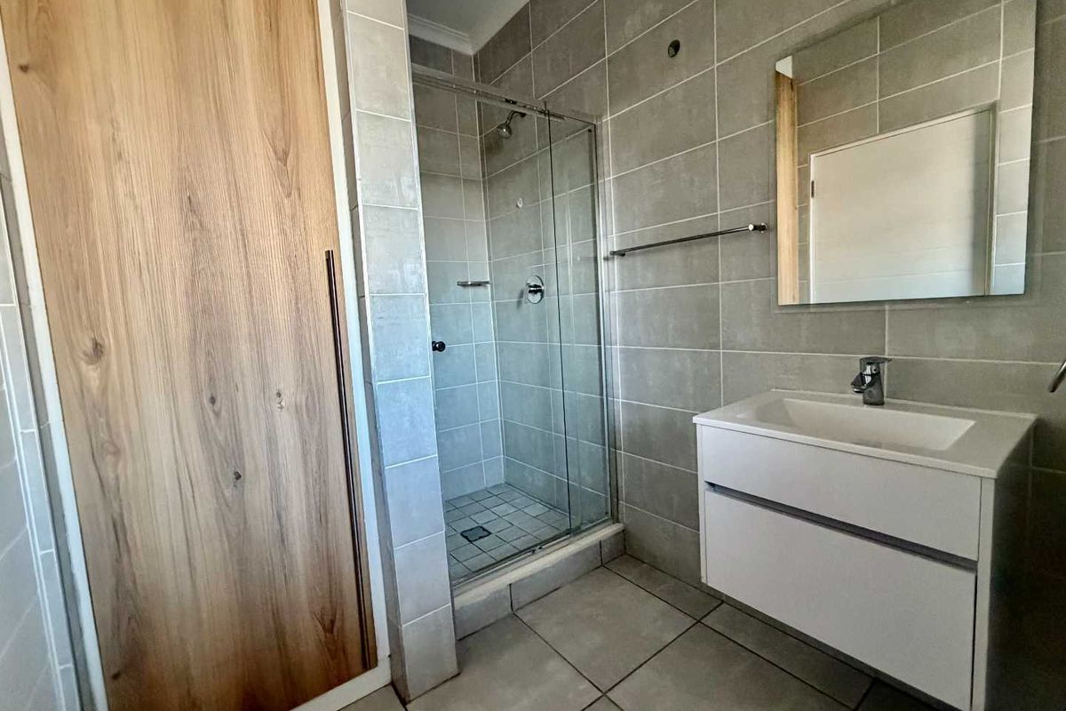 Modern bathroom featuring a glass shower enclosure, wall-mounted vanity with basin, and neutral grey wall and floor tiling.