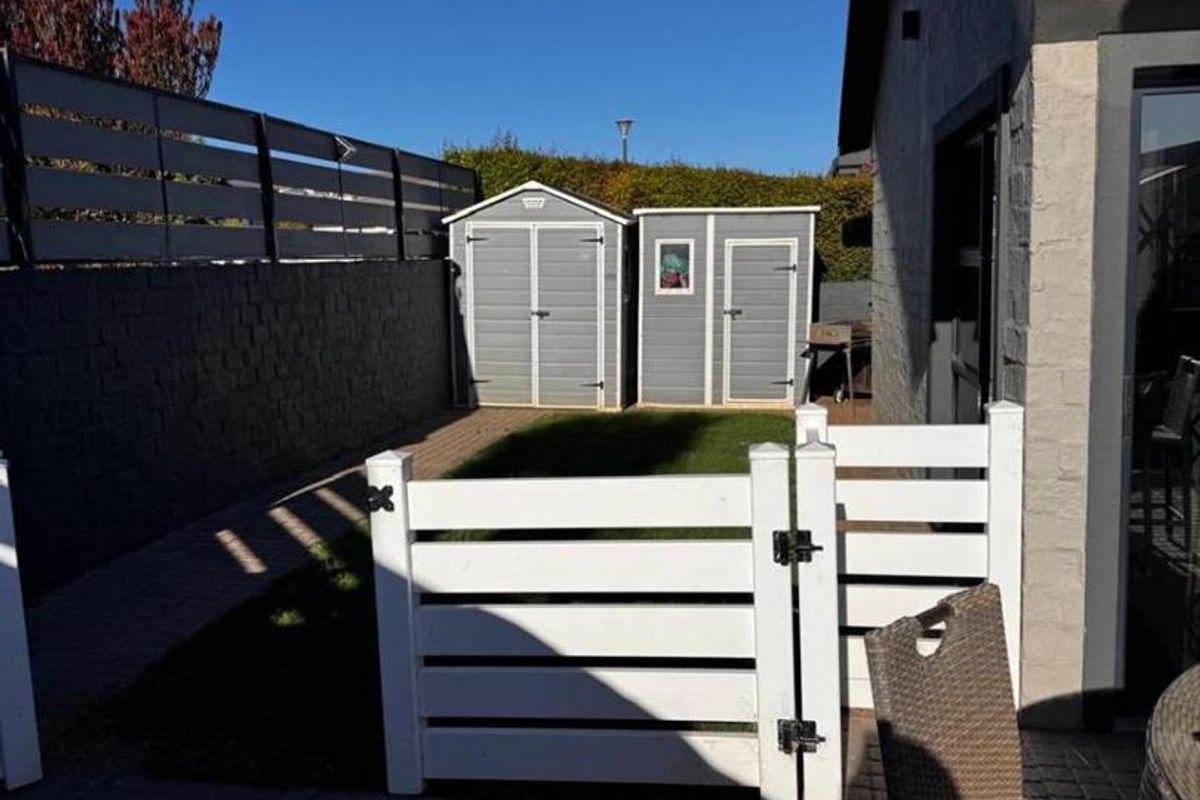 A private rear garden area featuring paved patio space, a small lawn, perimeter boundary walls, and two storage sheds.