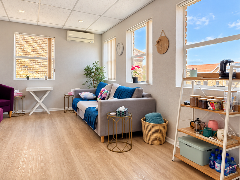 A bright and well-maintained office or lounge area featuring laminate flooring, a suspended ceiling with recessed lighting, and a wall-mounted air conditioning unit.