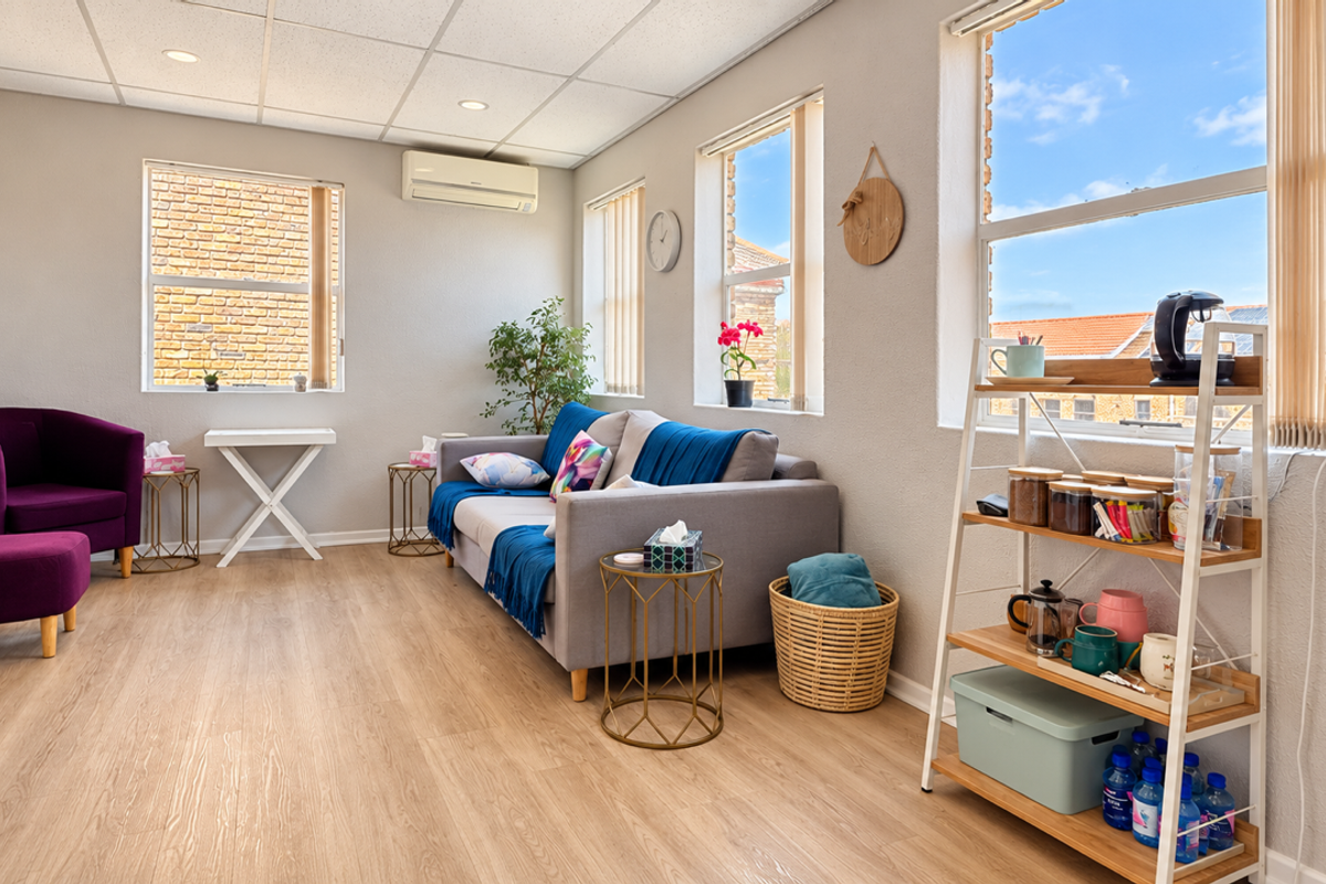A bright and well-maintained office or lounge area featuring laminate flooring, a suspended ceiling with recessed lighting, and a wall-mounted air conditioning unit.