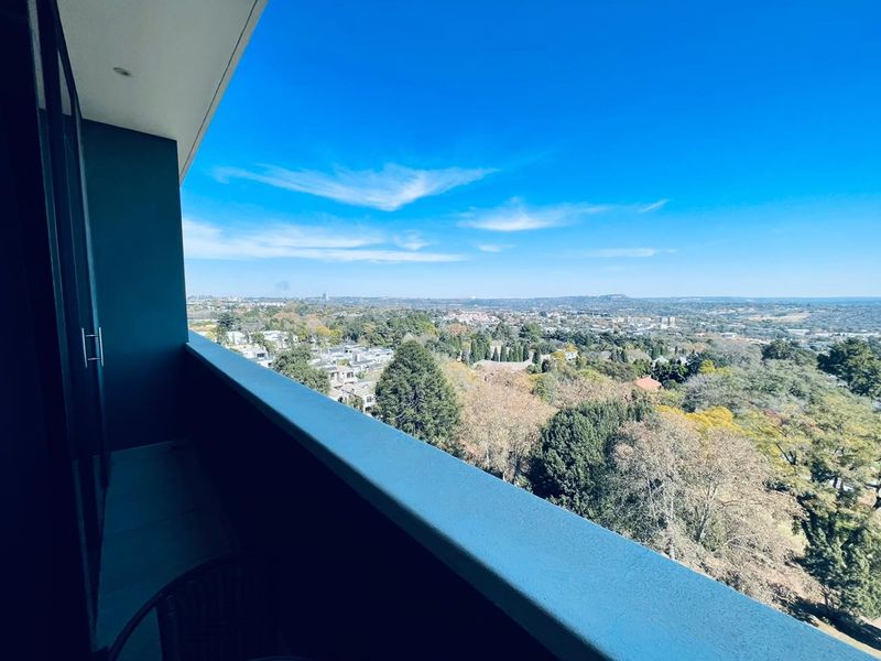 A private balcony featuring a modern railing and recessed lighting, offering expansive elevated views over the surrounding neighborhood and landscape.