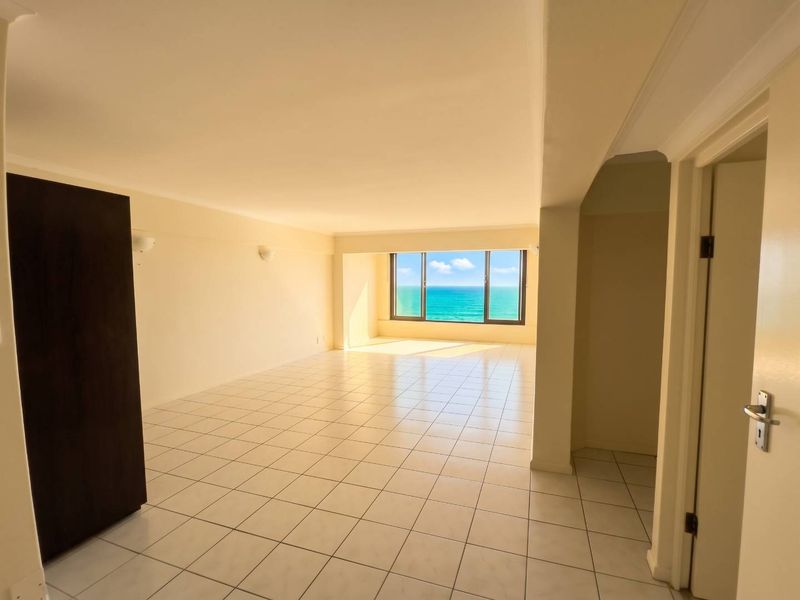 Spacious, empty living area featuring tiled flooring, built-in storage, and a large window offering a clear ocean view.