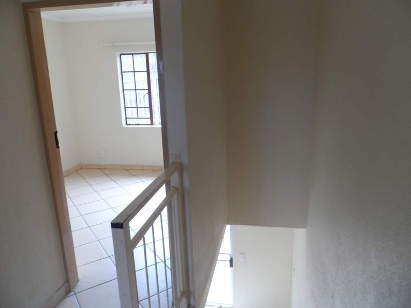 A view from the top of a staircase looking into an empty bedroom, featuring tiled flooring and a metal balustrade.