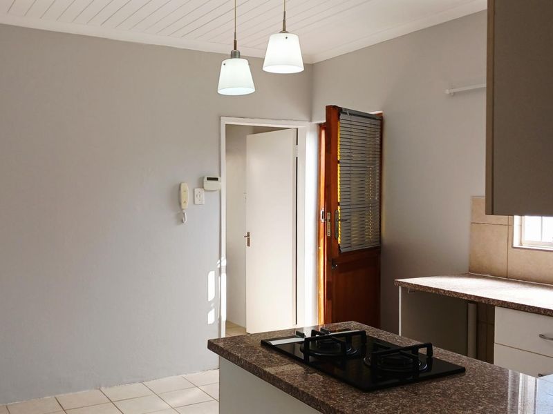 A clean, functional kitchen featuring granite countertops, a built-in gas hob, tiled flooring, and neutral wall finishes, offering a bright and practical workspace.