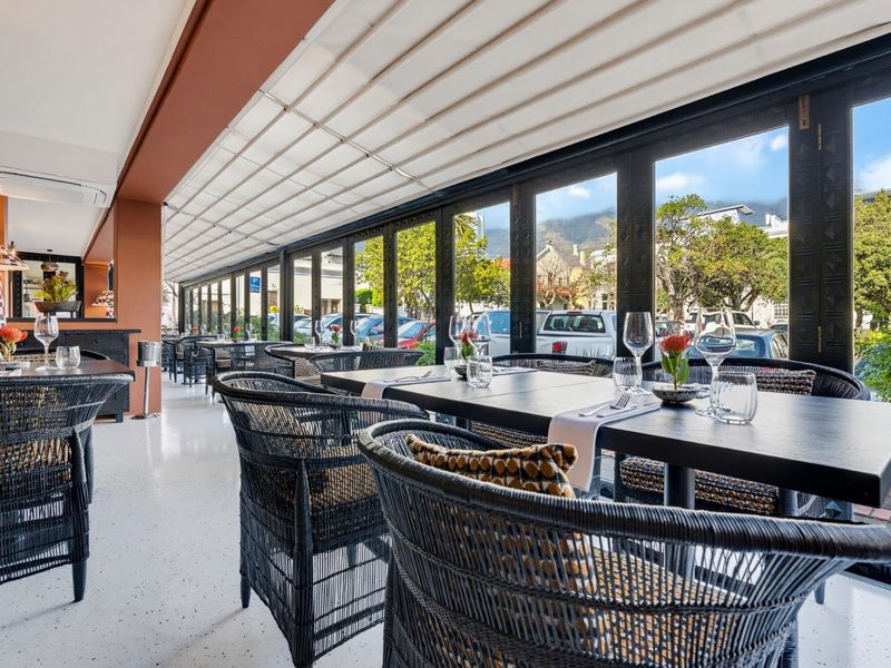 A modern, covered patio area featuring sleek terrazzo flooring, retractable overhead shading, and expansive folding glass doors that open to the street.