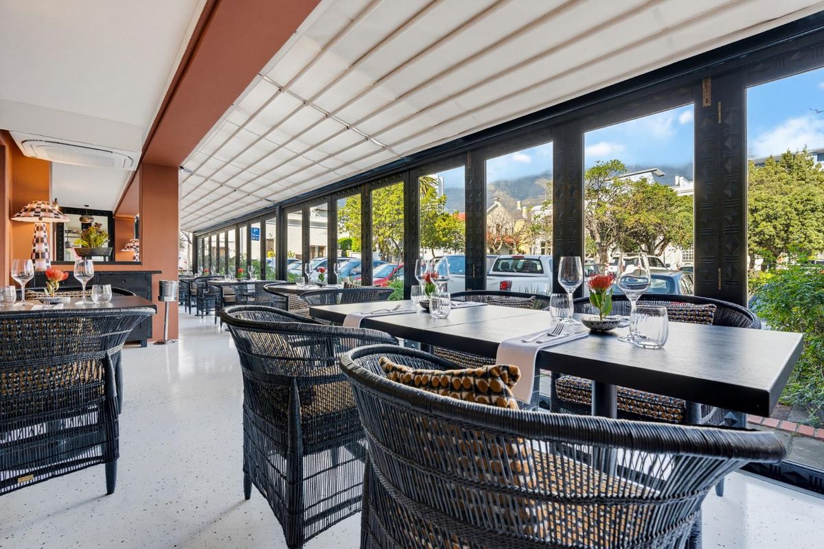 A modern, covered patio area featuring sleek terrazzo flooring, retractable overhead shading, and expansive folding glass doors that open to the street.