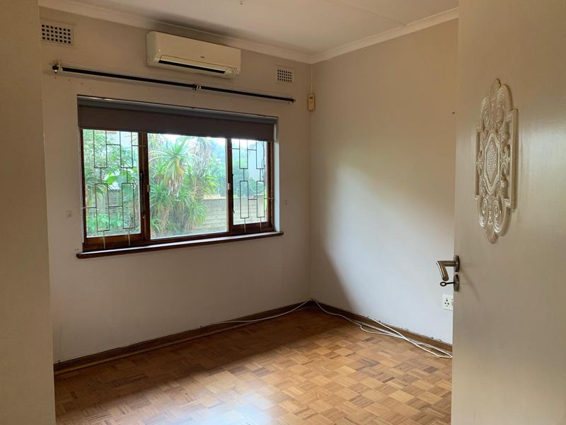 An empty bedroom featuring parquet flooring, a wall-mounted air conditioning unit, and a window fitted with security bars.