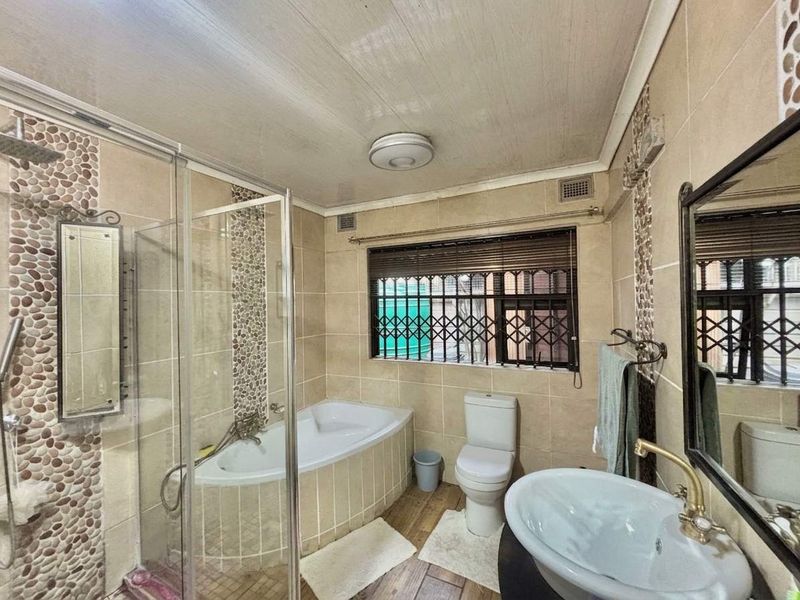 A functional bathroom featuring a glass shower enclosure, built-in bathtub, pedestal sink, and tiled walls with decorative pebble accents.
