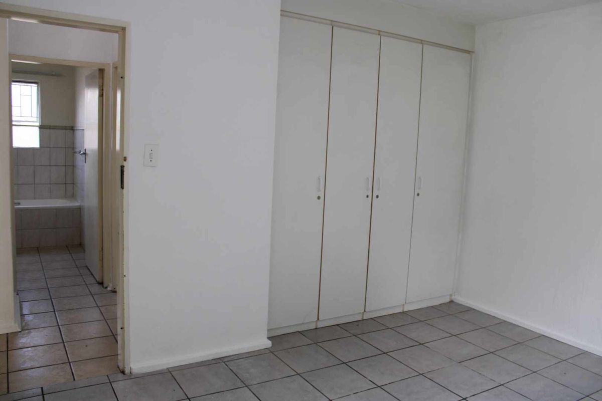 A bedroom featuring built-in cupboards and tiled flooring, with an adjacent view into a tiled bathroom.