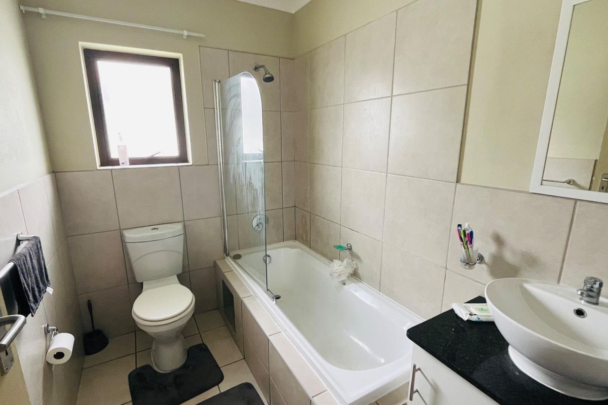 A functional bathroom featuring a bathtub with a glass shower screen, a vanity with a vessel sink, and neutral wall tiling.