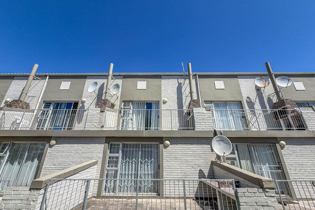 Rear exterior view of a multi-level apartment complex featuring brick facades, private balconies with metal railings, and ground-level patio areas.