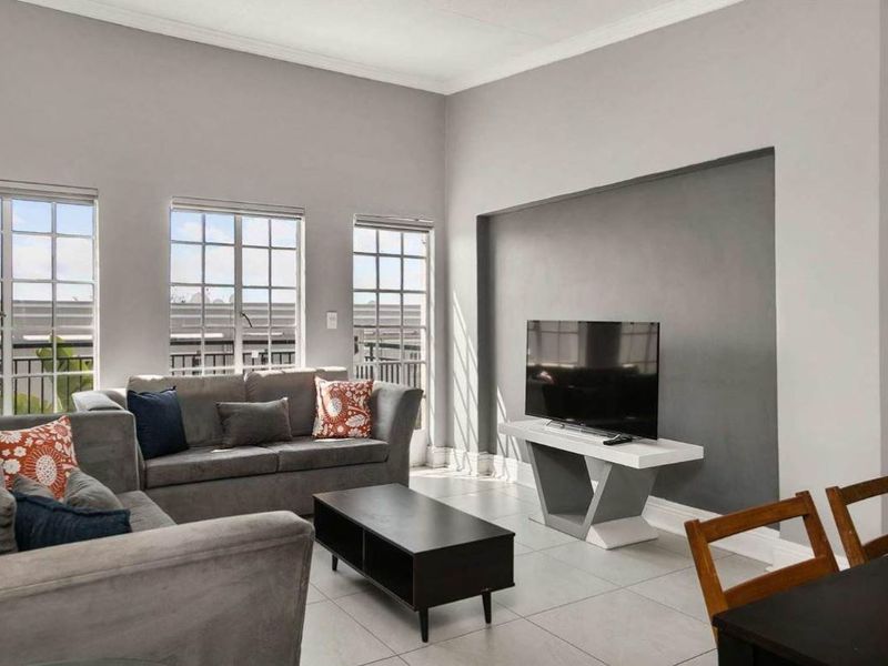 A bright and spacious living room featuring large multi-pane windows, neutral tiled flooring, and a modern recessed wall feature.