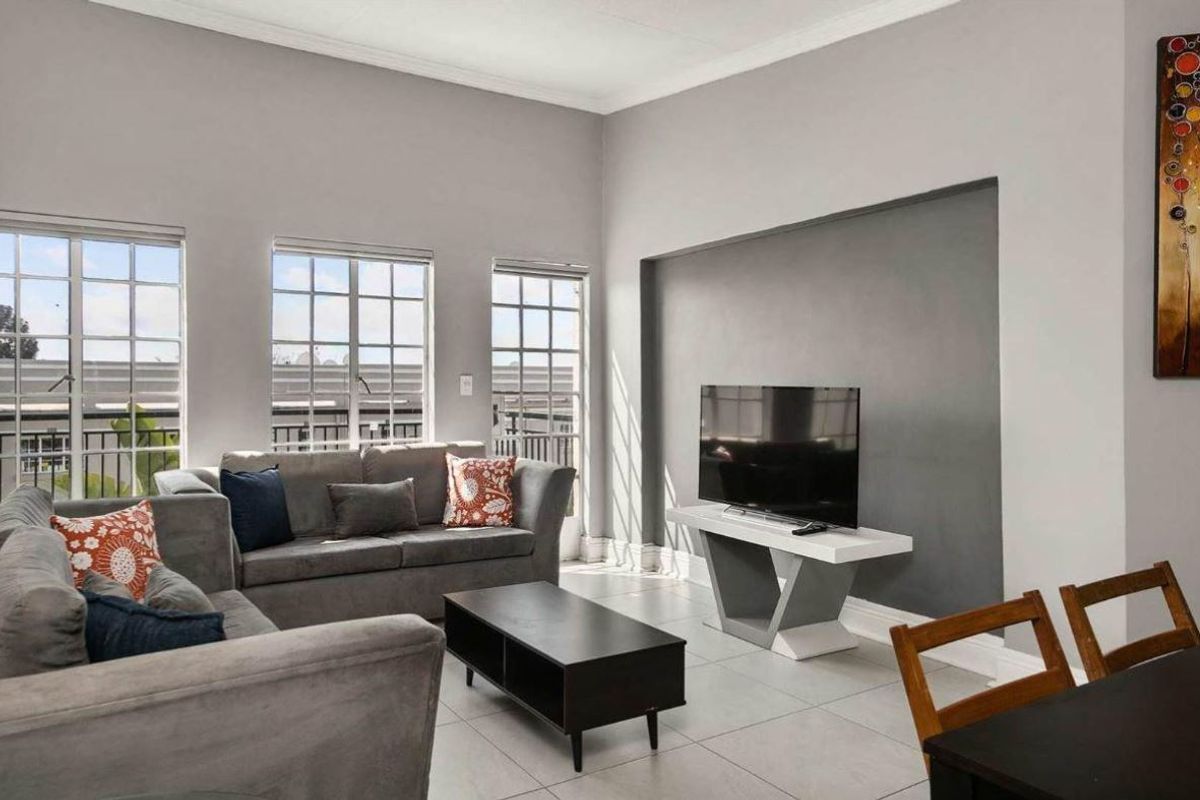 A bright and spacious living room featuring large multi-pane windows, neutral tiled flooring, and a modern recessed wall feature.