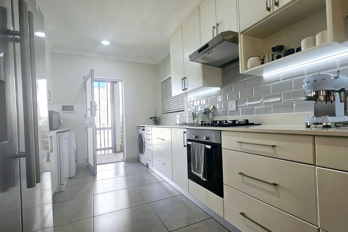 Modern kitchen featuring sleek cabinetry, subway tile backsplash, built-in oven and gas hob, with direct access to an outdoor area.