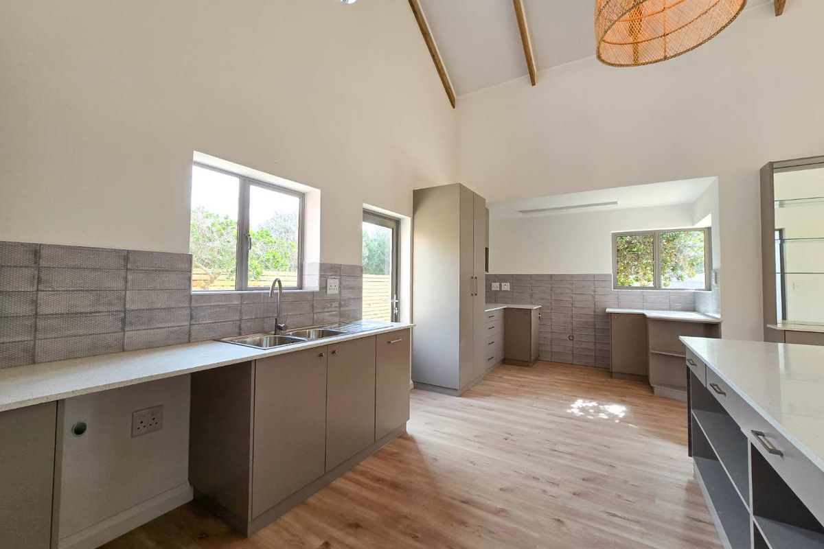 Modern kitchen featuring light wood-look flooring, neutral cabinetry, stone countertops, double sink, and high vaulted ceilings with exposed beams.