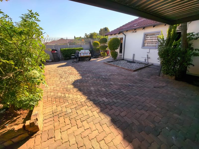 A paved rear courtyard area featuring a covered patio section, security fencing, and established garden borders.